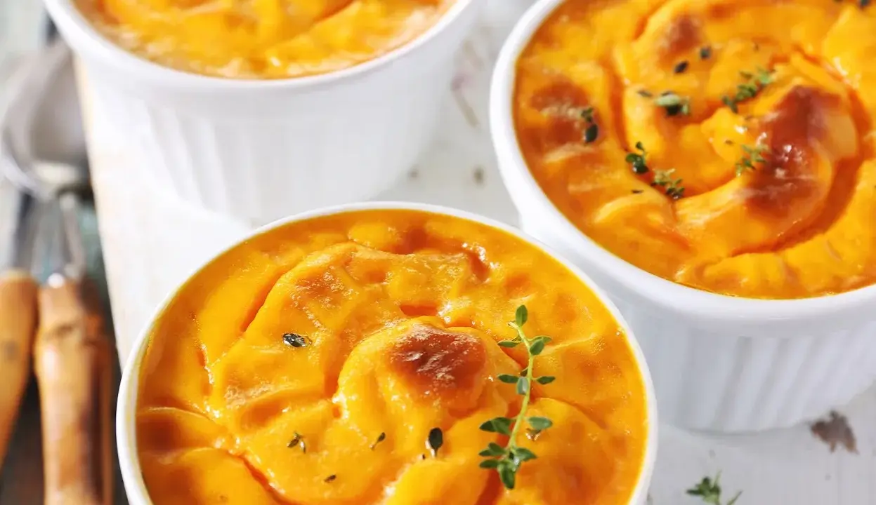 Trois ramequins de flan de butternut, dorés et garnis de thym frais, prêts à être dégustés.