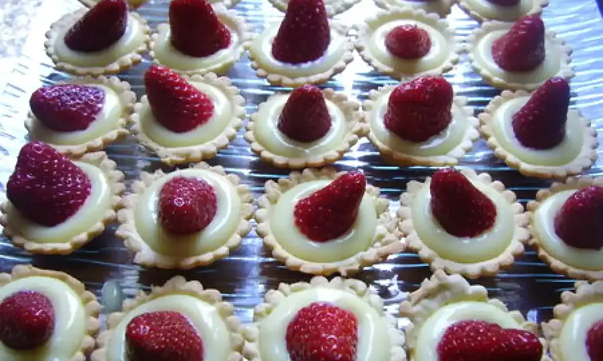 Une rangée de mini tartelettes fraise, garnies de crème pâtissière et d'une fraise rouge vif.