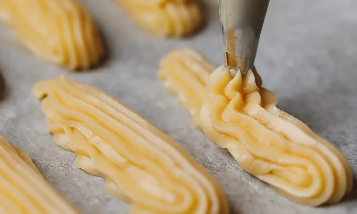 Pâte à choux traditionnelle dressée à la poche à douille sur une plaque de cuisson.