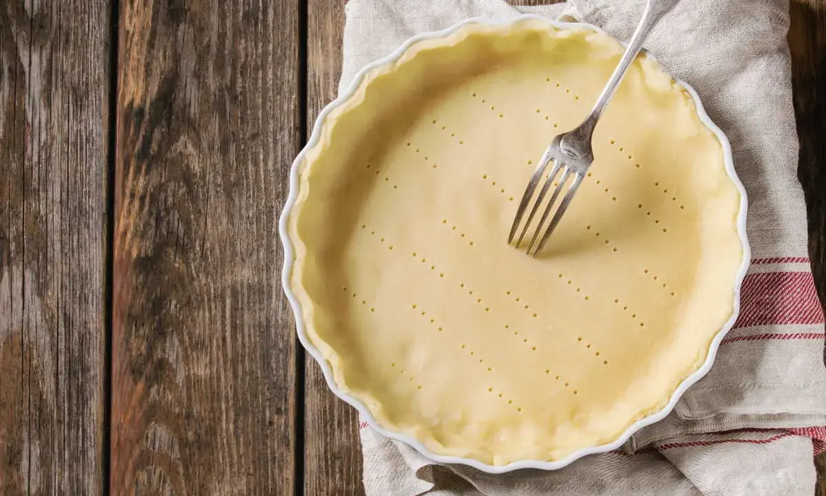 Pâte brisée sans beurre prête à être cuite dans un moule, avec une fourchette plantée dedans. Parfait pour une tarte légère.
