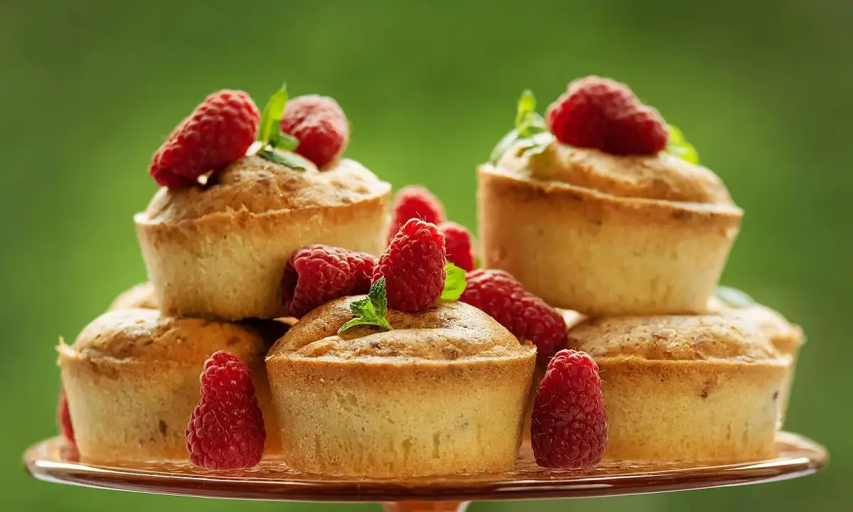 Délicieux financiers pistache framboise empilés sur un plateau, ornés de framboises fraîches et de feuilles de menthe.