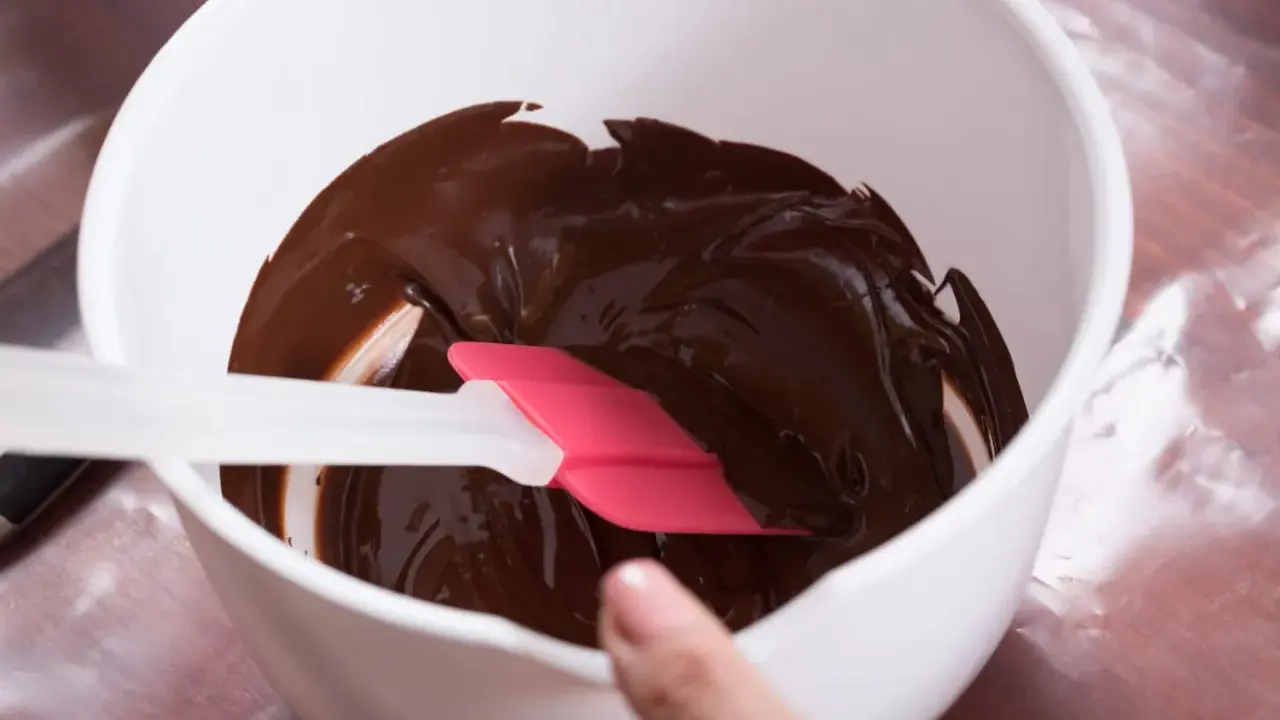 Comment faire fondre du chocolat : une spatule rose et blanche mélange du chocolat fondu brillant dans un bol blanc.