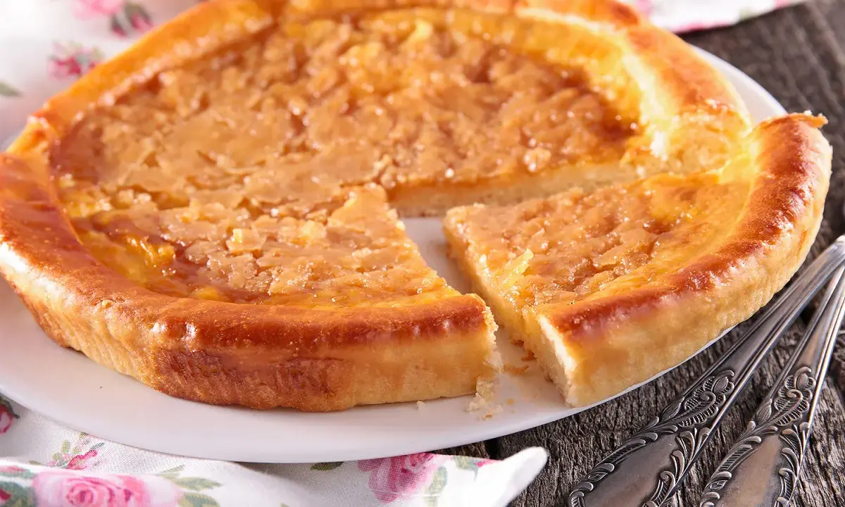 Une délicieuse tarte à la cassonade, dorée et appétissante, est servie sur une assiette blanche, prête à être dégustée avec des couverts ornés.