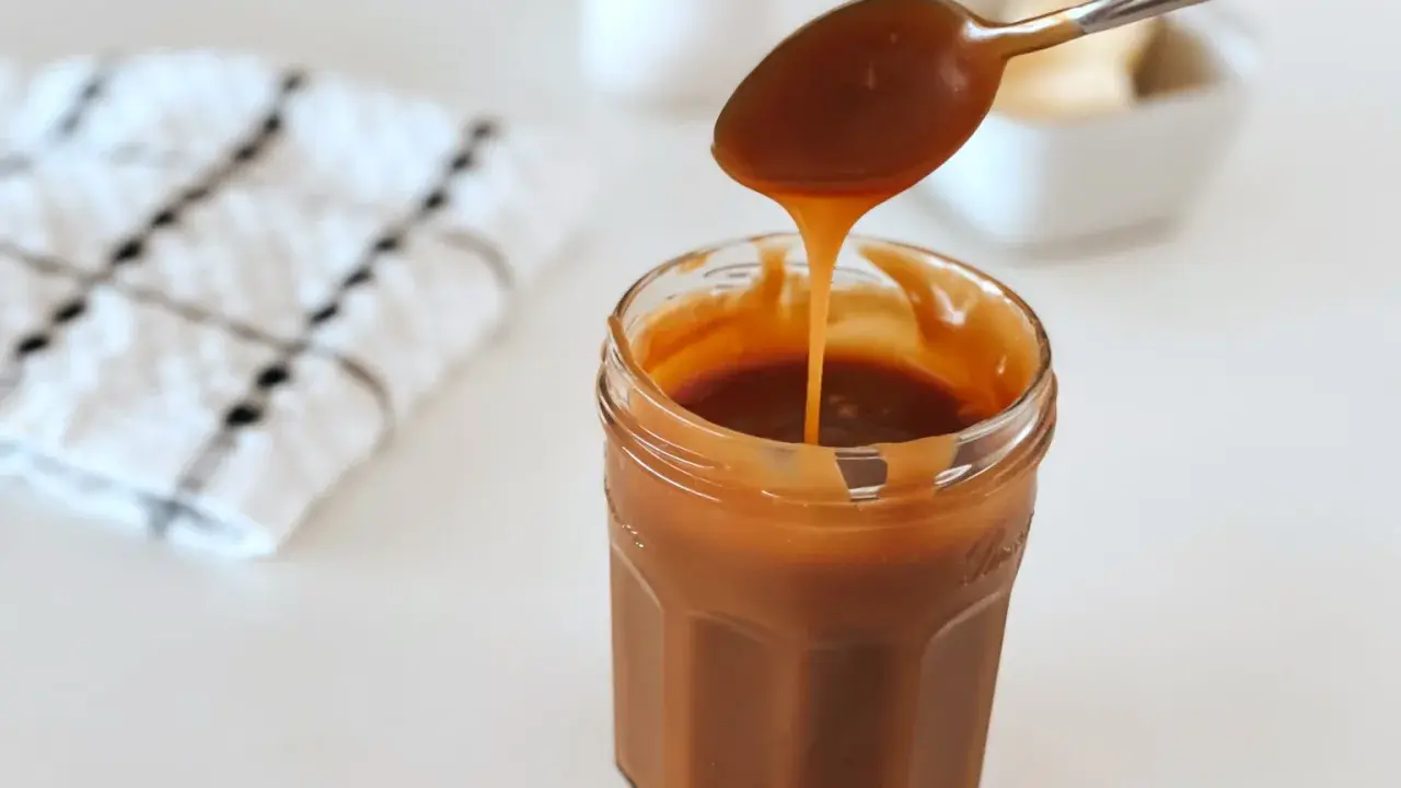 Une cuillère verse du caramel beurre salé dans un pot. Le beurre doux est visible en arrière-plan.