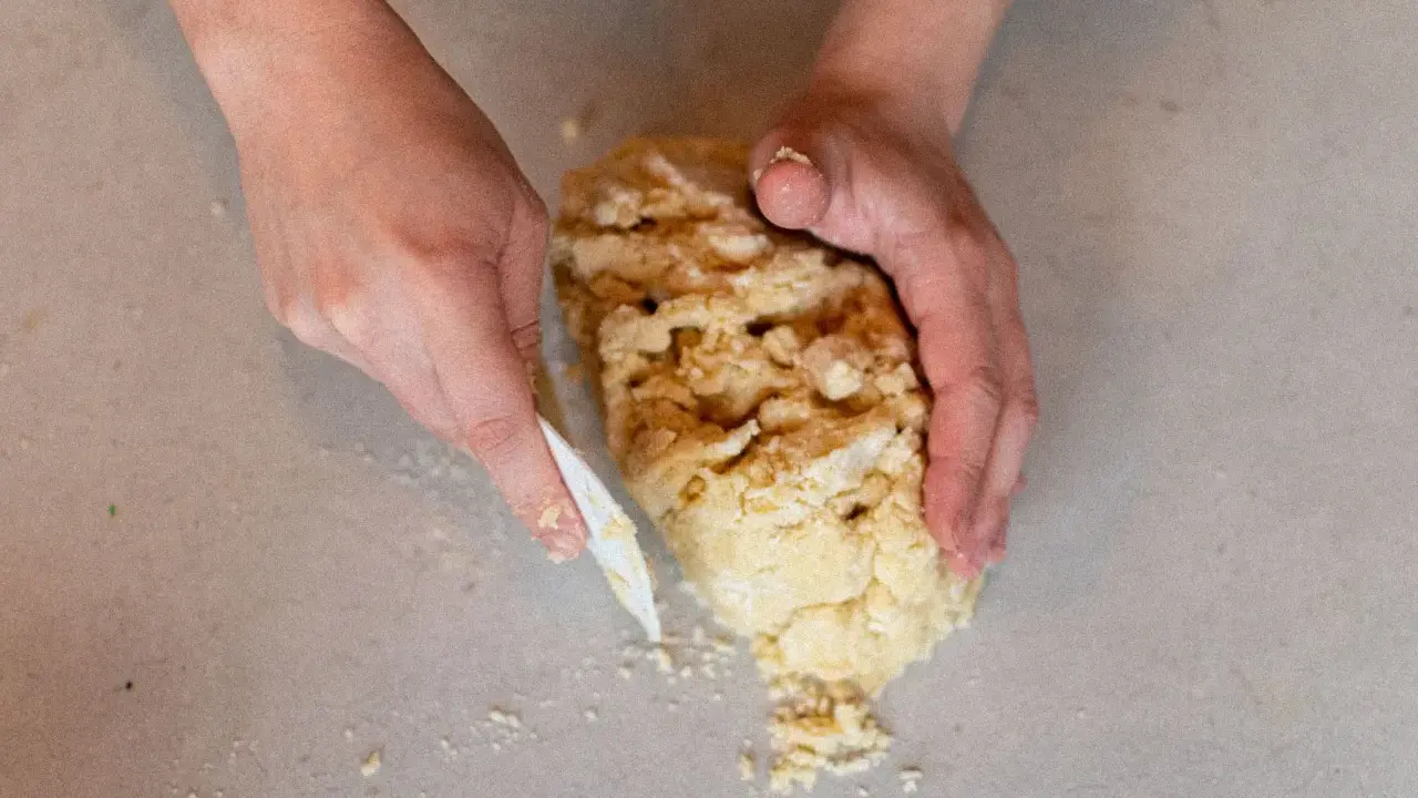 Mains travaillant une pâte sablée pour une recette de pâte sucrée. La pâte est friable et en cours de formation.