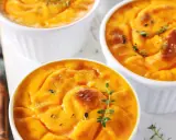 Trois ramequins de flan de butternut, dorés et garnis de thym frais, prêts à être dégustés.