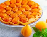 Tarte aux abricots caramélisés sur un fond de tarte croustillant, avec des abricots frais et des feuilles de basilic sur le côté.