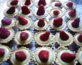 Une rangée de mini tartelettes fraise, garnies de crème pâtissière et d'une fraise rouge vif.