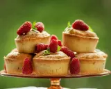 Délicieux financiers pistache framboise empilés sur un plateau, ornés de framboises fraîches et de feuilles de menthe.