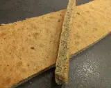 Un biscuit joconde noisette, fin et doré, est coupé en deux. Une fine tranche repose sur une plus grande pièce.