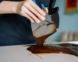 Mains travaillant du chocolat brillant sans tempérage avec des spatules. La texture fondante et lustrée promet une gourmandise parfaite.