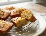 Délicieux financier aux noisettes, dorés et parsemés d'amandes effilées, sur une grille. L'un est coupé, révélant sa mie moelleuse.