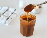Une cuillère verse du caramel beurre salé dans un pot. Le beurre doux est visible en arrière-plan.