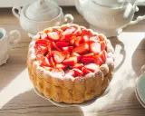 Gâteau frais garni de fraises, entouré de biscuits cuillère et saupoudré de sucre glace. Une belle table de thé.