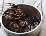 Fouet mélangeant du chocolat noir brillant dans une casserole, étape clé pour le tempérage.