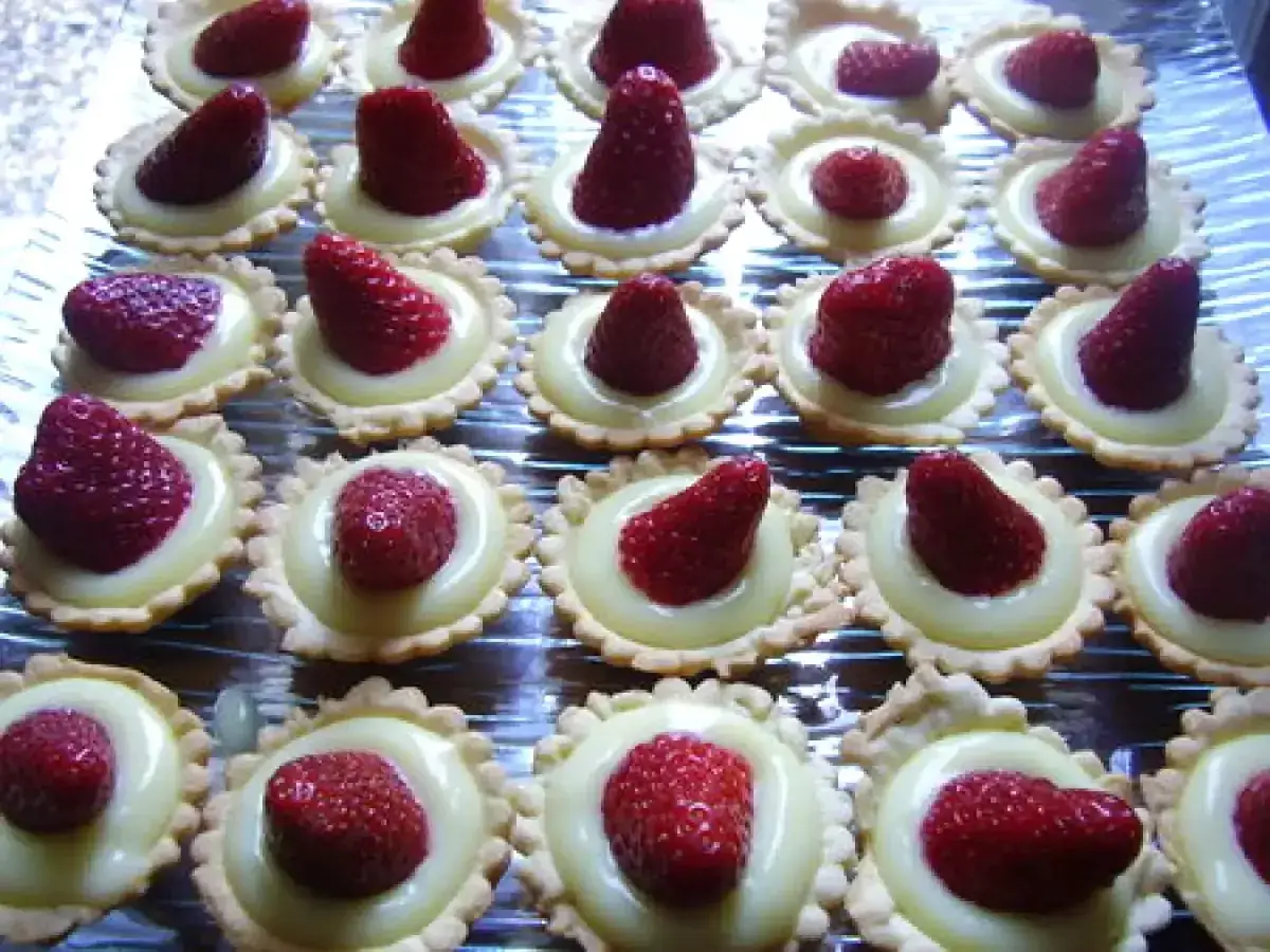 Une rangée de mini tartelettes fraise, garnies de crème pâtissière et d'une fraise rouge vif.
