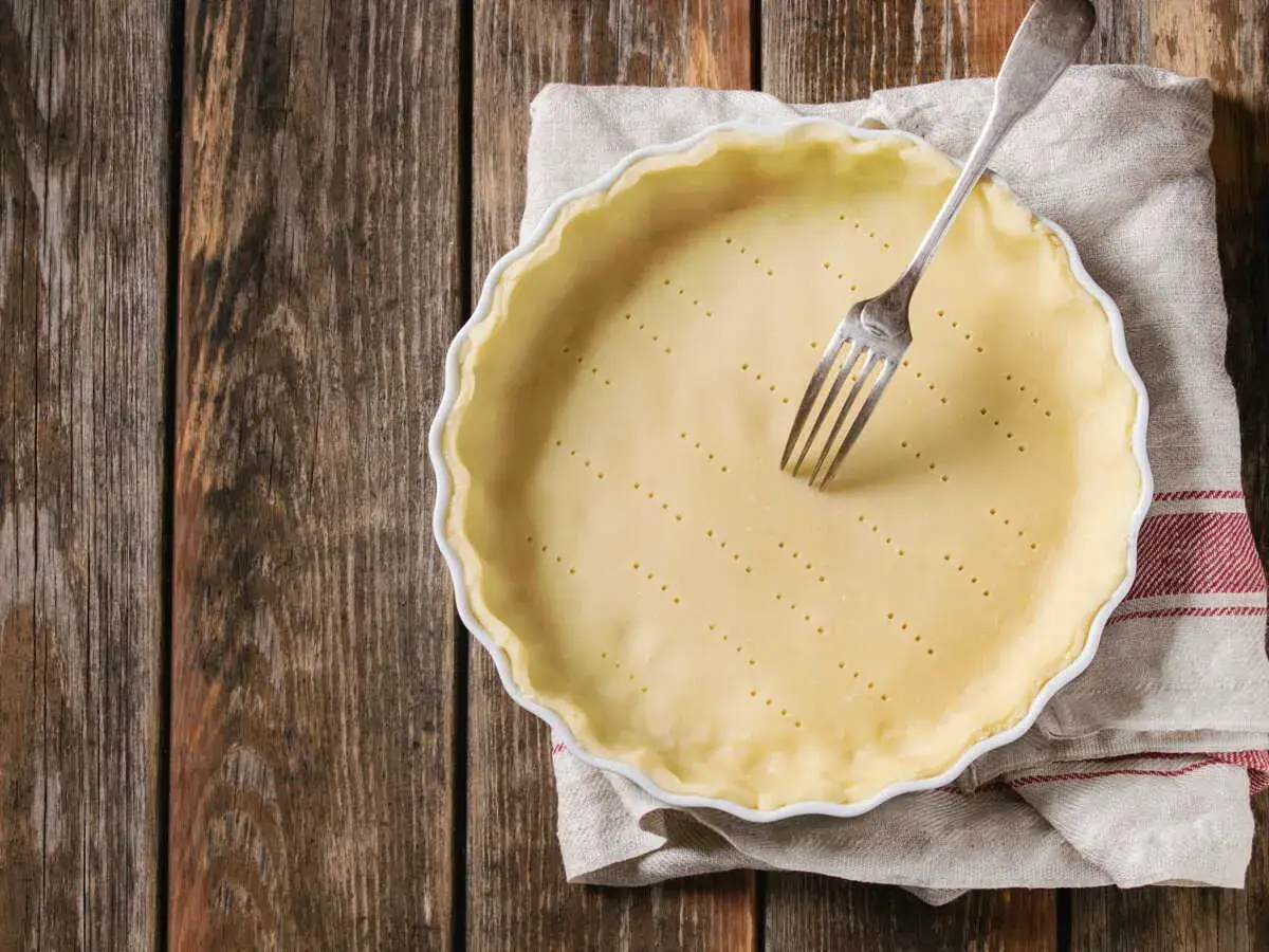 Pâte brisée sans beurre prête à être cuite dans un moule, avec une fourchette plantée dedans. Parfait pour une tarte légère.