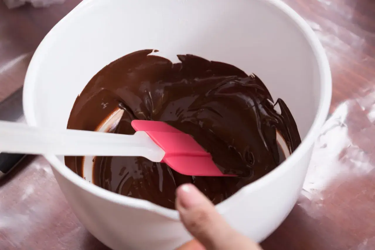 Comment faire fondre du chocolat : une spatule rose et blanche mélange du chocolat fondu brillant dans un bol blanc.