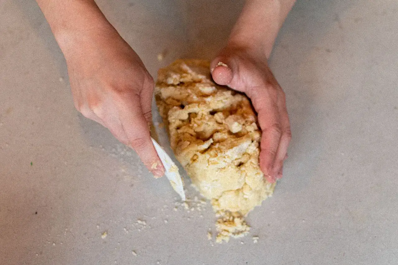 Mains travaillant une pâte sablée pour une recette de pâte sucrée. La pâte est friable et en cours de formation.