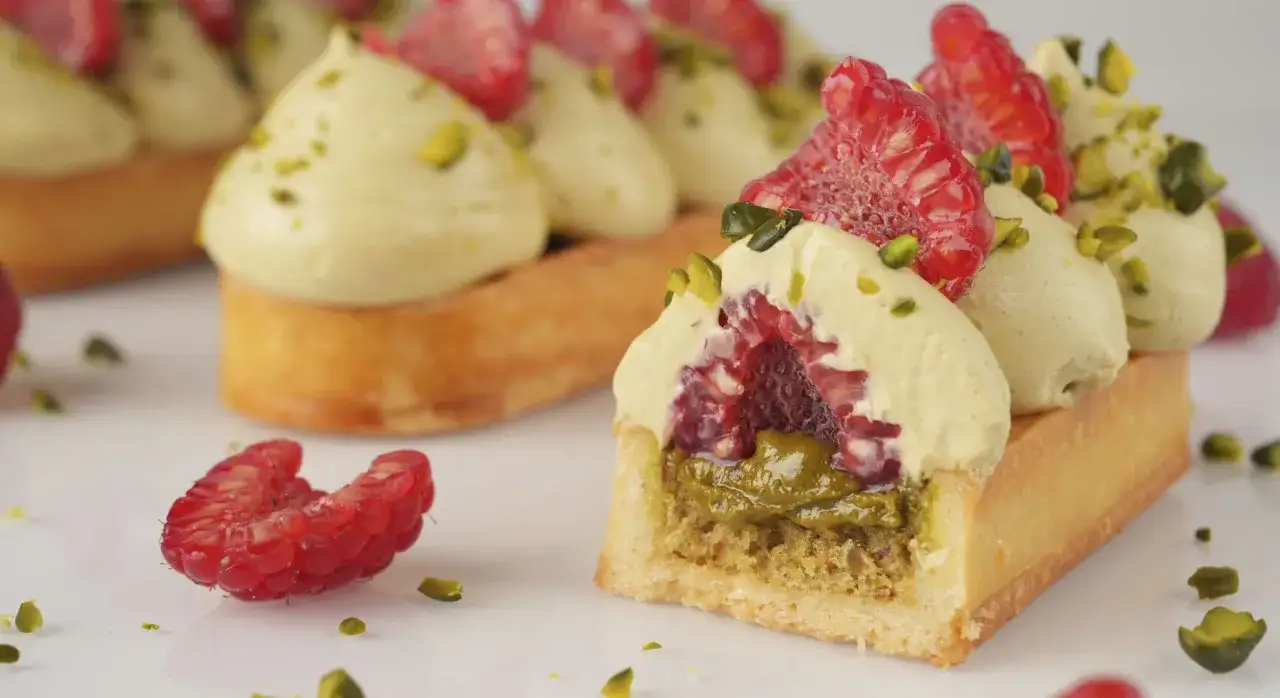 Délicieuse recette tarte pistache framboise : une pâte sablée garnie de crème pistache, framboises fraîches et éclats de pistaches.