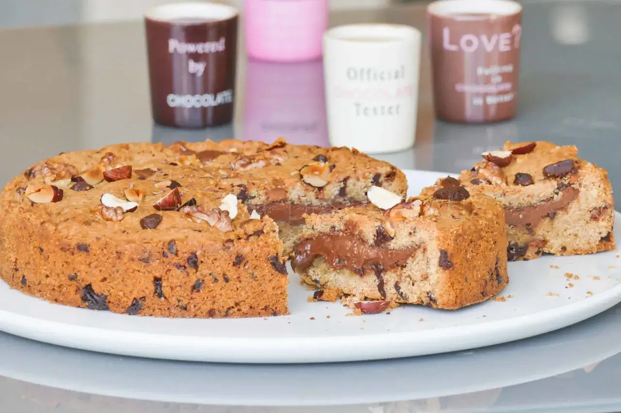 Gâteau cookie moelleux garni de Nutella, parsemé de noisettes et pépites de chocolat. Un délice gourmand !