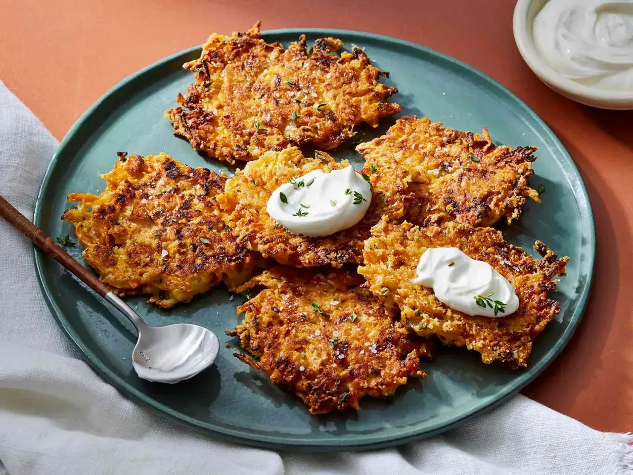 Cinq beignets de butternut dorés et croustillants, garnis de crème aigre et de thym, sur une assiette verte.