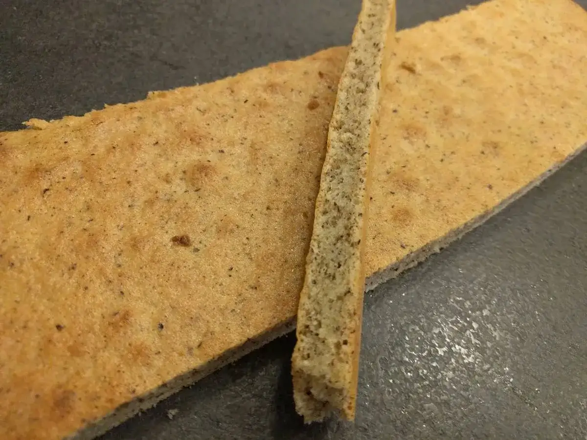 Deux fines plaques de biscuit madeleine pour entremet, l'une posée sur l'autre, sur fond sombre.
