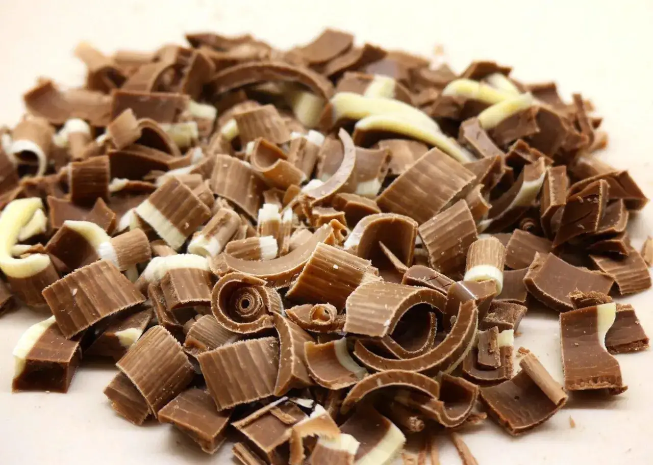 Un tas de copeaux de chocolat au lait et blanc, prêts à être utilisés pour comment râper du chocolat sur un gâteau.
