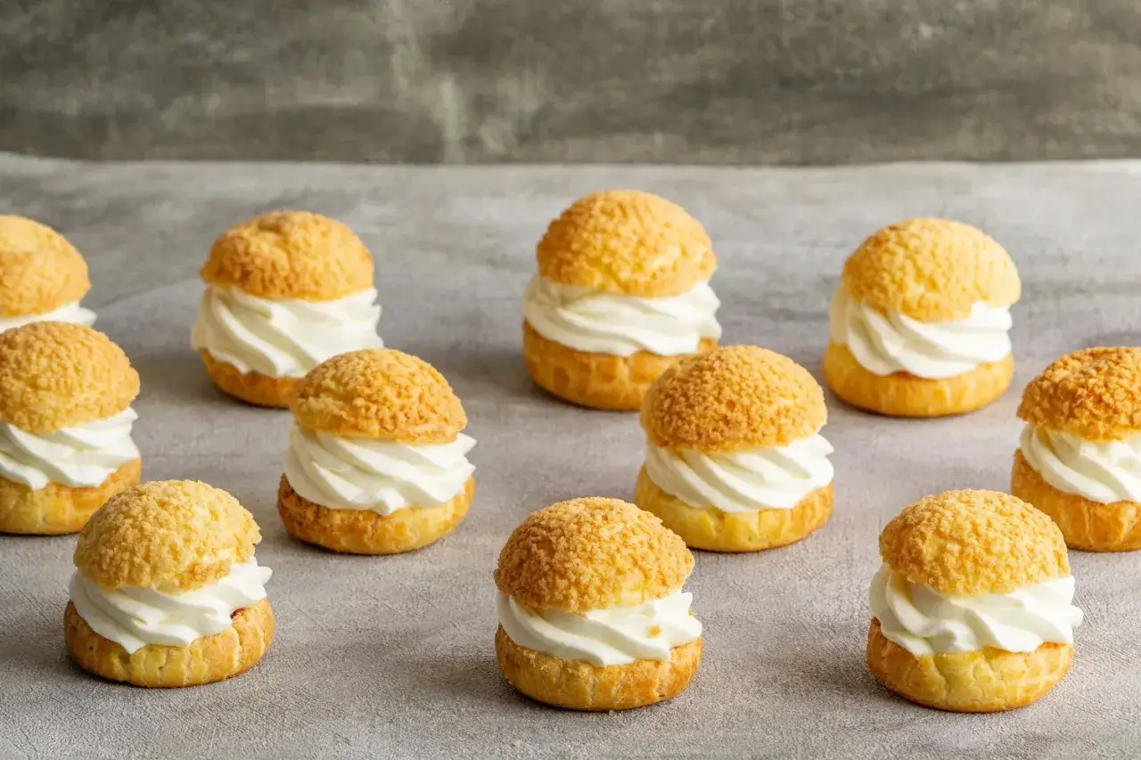 Douze petits choux garnis de crème fouettée, prêts à être dégustés. Une recette pâte à choux traditionnelle réussie.