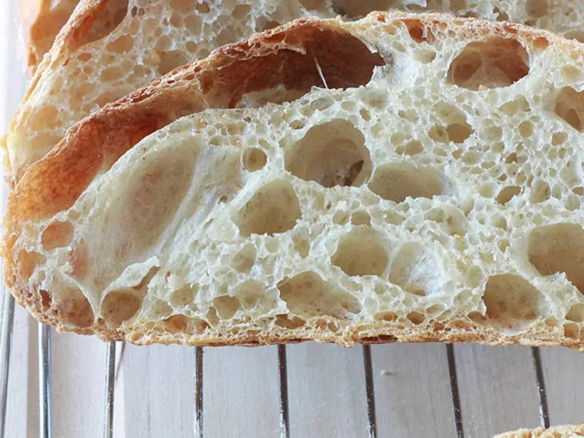 Tranches de pain artisanal avec une mie aérée et de grandes alvéoles, parfaites pour savoir comment obtenir un pain très alvéolé.