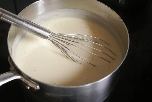Une béchamel onctueuse se prépare dans une casserole avec un fouet. 1 litre de lait mijote doucement.