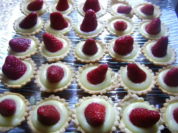 Une rangée de mini tartelettes fraise, garnies de crème pâtissière et d'une fraise rouge vif.