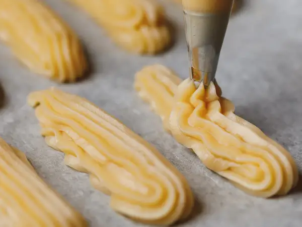 Pâte à choux traditionnelle dressée à la poche à douille sur une plaque de cuisson.