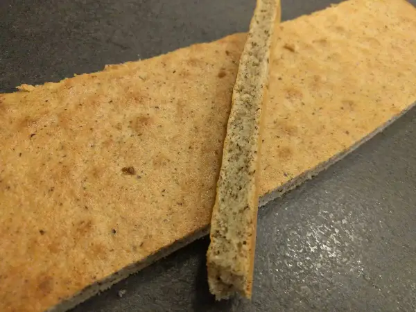 Un biscuit joconde noisette, fin et doré, est coupé en deux. Une fine tranche repose sur une plus grande pièce.