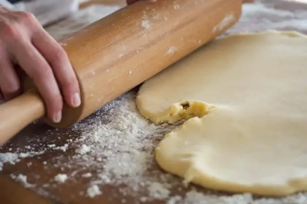 Mains roulant une pâte à biscuits trop sableux. Farine saupoudrée sur la planche en bois.