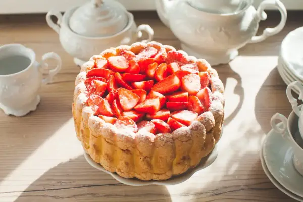 Gâteau frais garni de fraises, entouré de biscuits cuillère et saupoudré de sucre glace. Une belle table de thé.