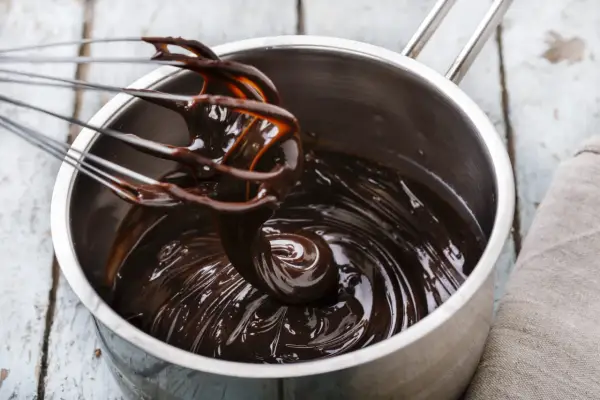 Fouet mélangeant du chocolat noir brillant dans une casserole, étape clé pour le tempérage.