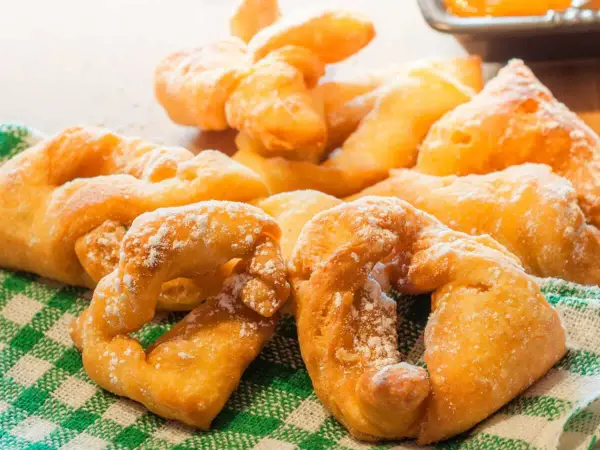 Beignets dorés saupoudrés de sucre glace sur un torchon à carreaux verts.