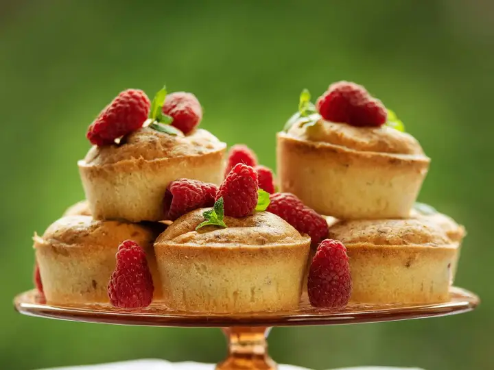 Délicieux financiers pistache framboise empilés sur un plateau, ornés de framboises fraîches et de feuilles de menthe.