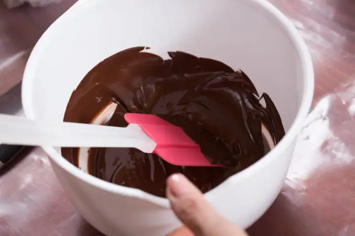Comment faire fondre du chocolat : une spatule rose et blanche mélange du chocolat fondu brillant dans un bol blanc.