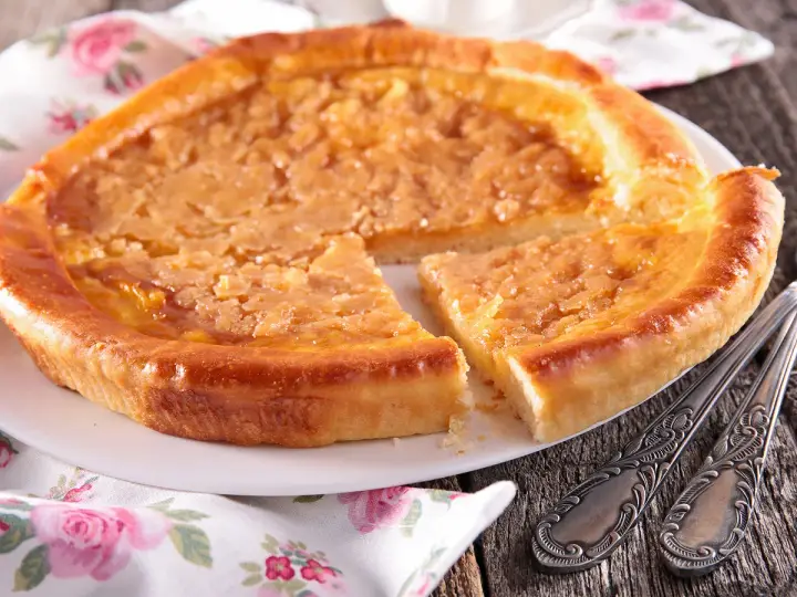 Une délicieuse tarte à la cassonade, dorée et appétissante, est servie sur une assiette blanche, prête à être dégustée avec des couverts ornés.