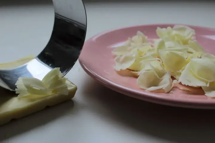 Un ustesile en métal crée des copeaux de chocolat blanc sur une assiette rose.