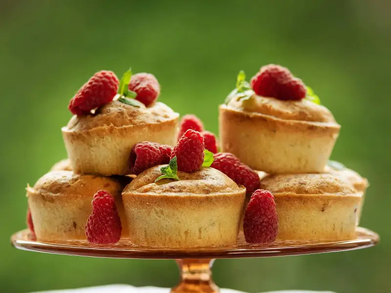 Délicieux financiers pistache framboise empilés sur un plateau, ornés de framboises fraîches et de feuilles de menthe.