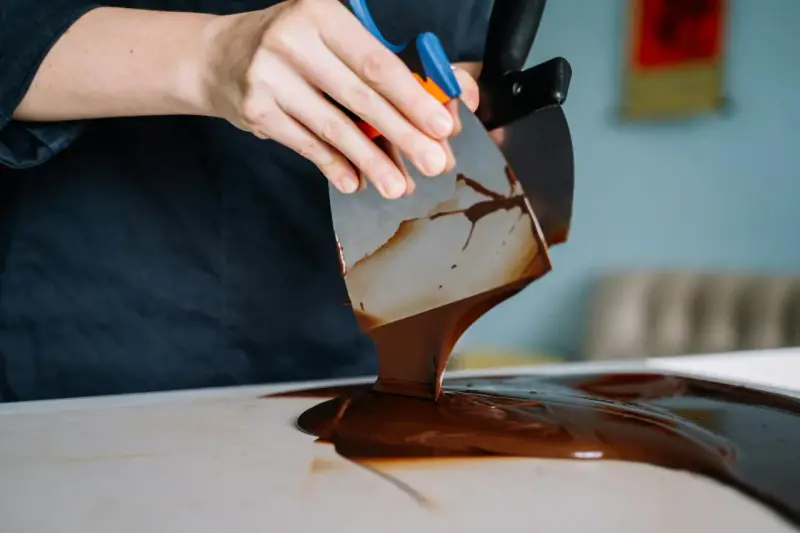 Mains travaillant du chocolat brillant sans tempérage avec des spatules. La texture fondante et lustrée promet une gourmandise parfaite.