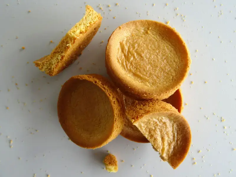 Des morceaux de sablé breton moelleux, certains entiers, d'autres brisés, éparpillés sur un fond clair.